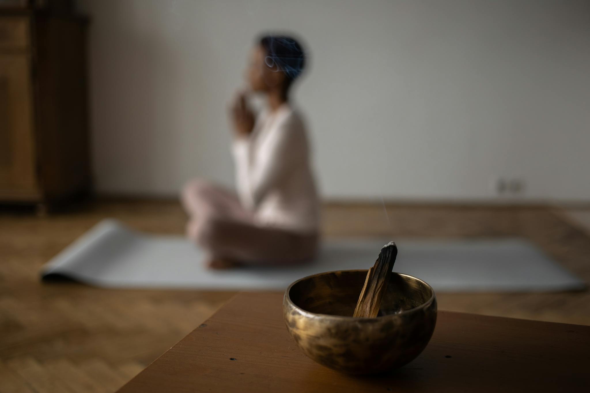A serene indoor scene of meditation with an incense bowl and a woman practicing yoga.