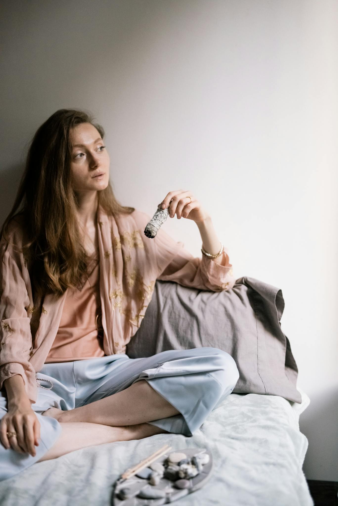 A woman holding sage while meditating indoors, creating a peaceful atmosphere.